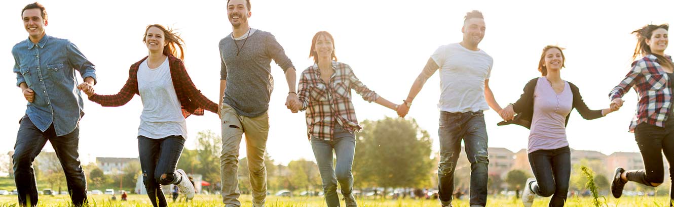 Group of people smiling while they hold hands in the meadow.